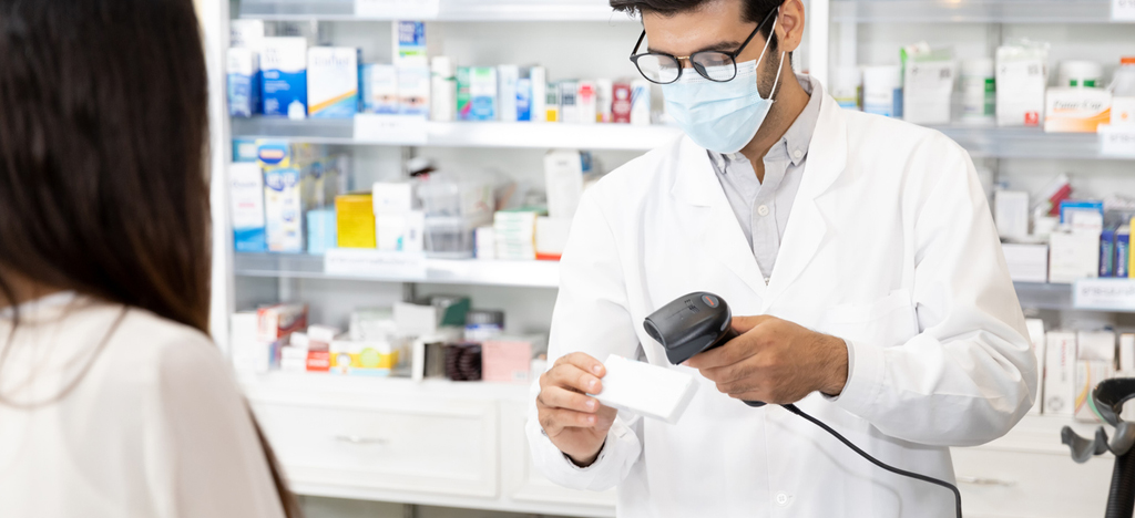 A male pharmacist is scanning the medication’s barcode for a buyer.