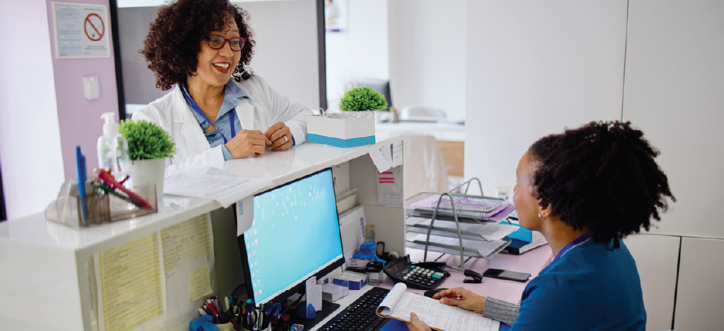 Using automated medical billing software - A female doctor speaking with a female medical staff who is in charge of patient billing.
