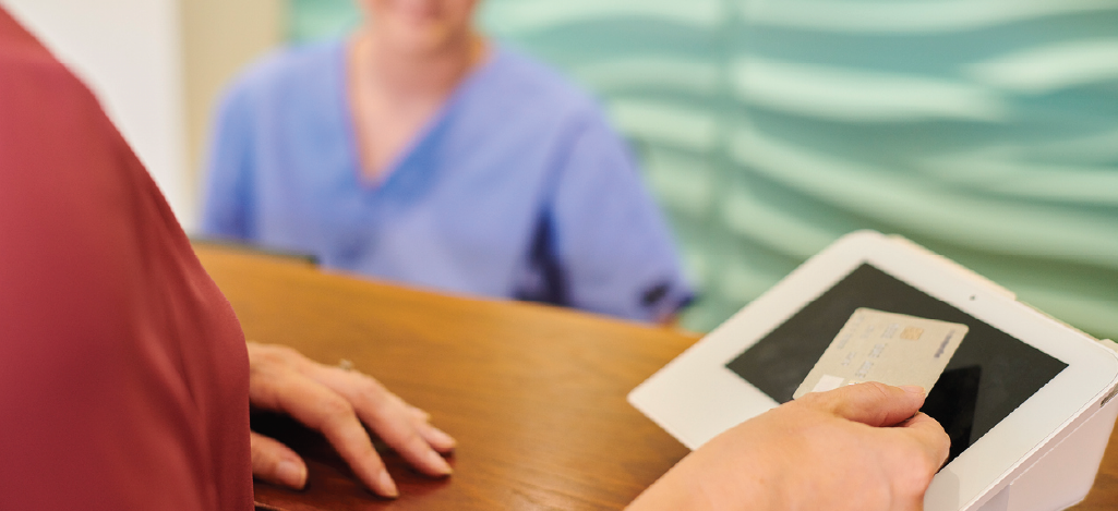 Healthcare payment processing - Woman scanning her credit card in front of a nurse at a reception area.
