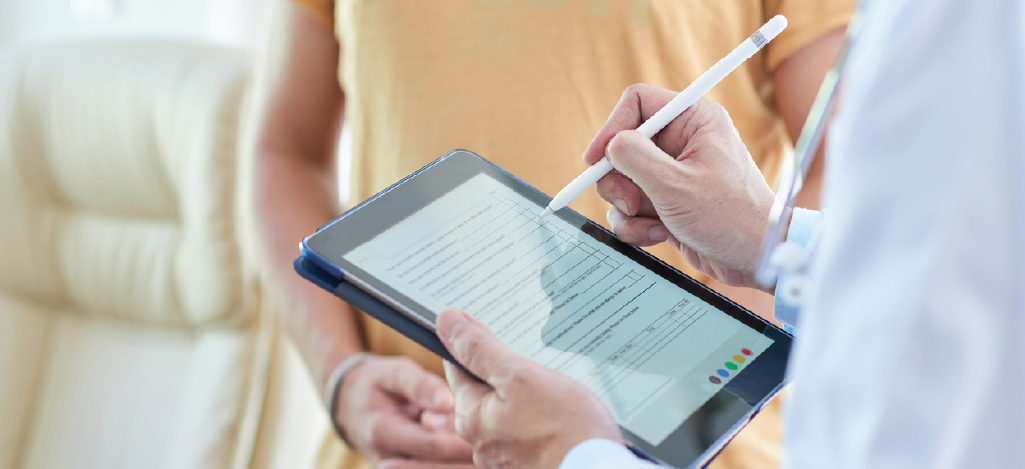 Doctor using a digital tablet to record treatment information in front of his patient.