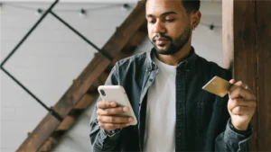 Man looking at his phone with his card in hand using healthcare payment solutions to pay a bill