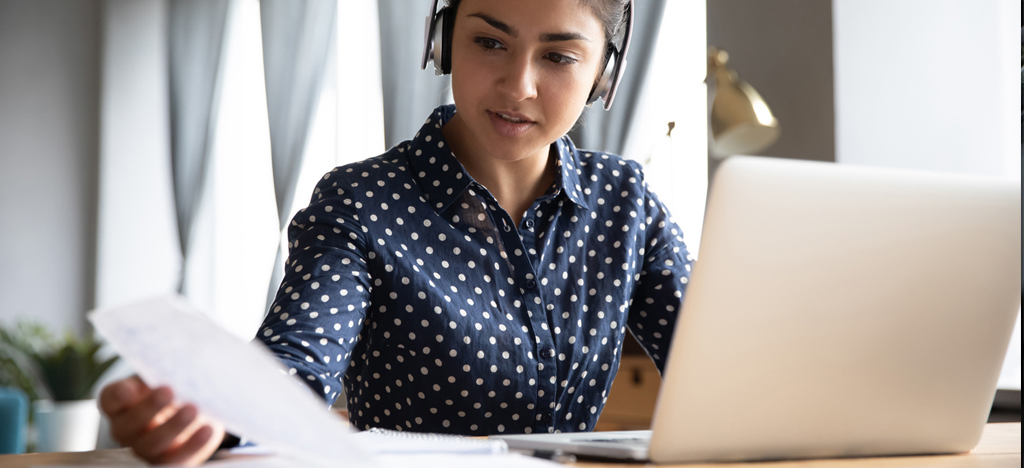 Shot of a young lady working on her laptop while wearing headphones.