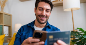 Text to Pay - A man at home using his smartphone and credit card to pay for his medical bill online.