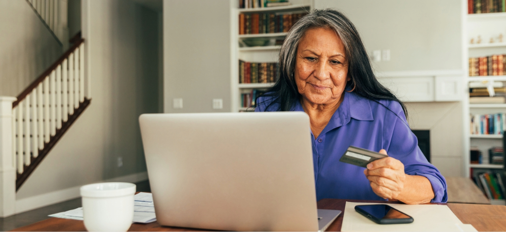 End-to-end RCM software - A senior woman at home paying her medical bills using her laptop and credit card.