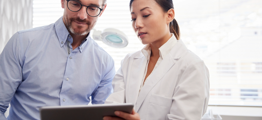 A female doctor using a tablet device while explaining surgery procedures to her male patient.