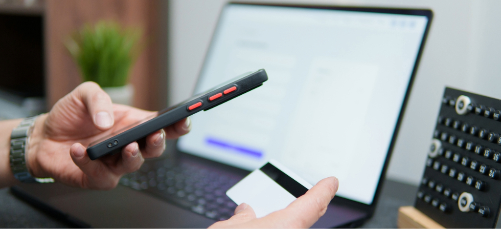 Rev cycle management - A man at home using his laptop, smartphone, and credit card to settle his medical bill.