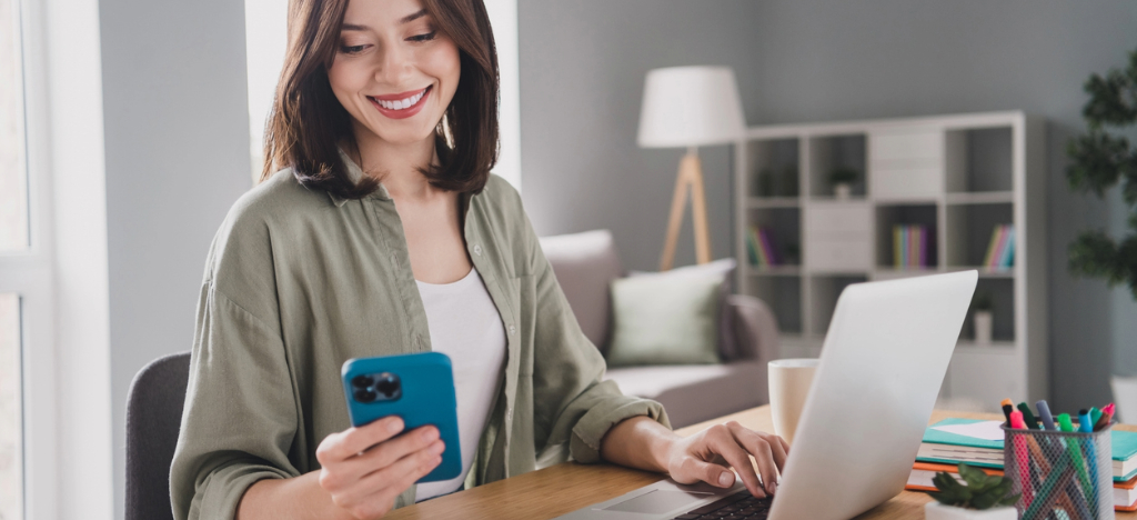 A woman at home reviewing her medical bills using a smartphone and laptop.