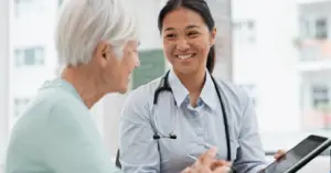 Providing flexible payment plans to patients - A female doctor holding a tablet device while speaking to a senior patient.