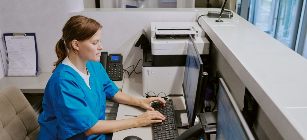 Female medical office staff working at a reception desktop computer.