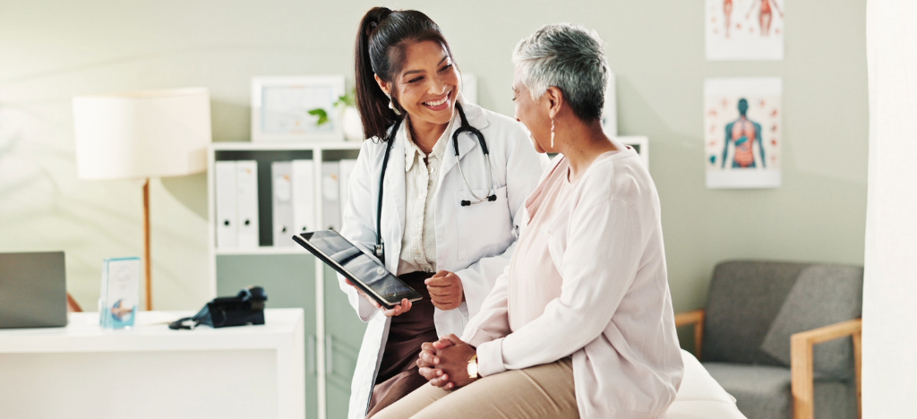 A female doctor holding a tablet device while explaining payment options to her senior female patient.