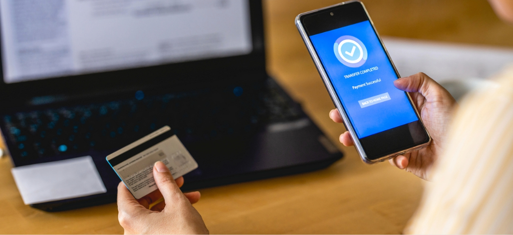 HIPAA-compliant text messaging - A woman at home using her laptop, smartphone, and credit card to pay for her medical bills online.