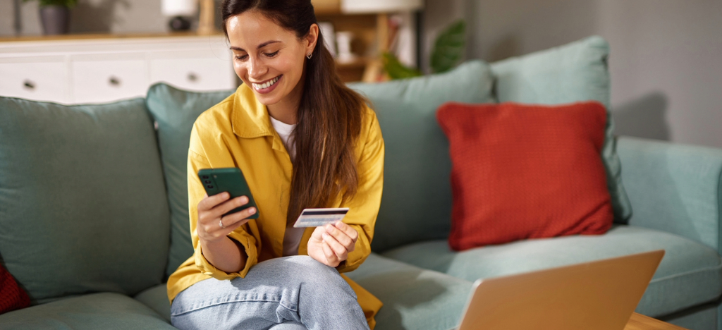 High-deductible health plans - A woman at home using her smartphone and credit card to pay for her medical bills.