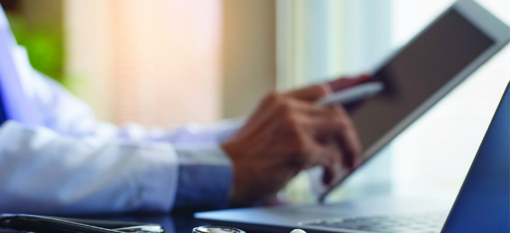 Pre-visit billing for medical practices - A male doctor using a tablet device and laptop to check patients’ electronic bills.