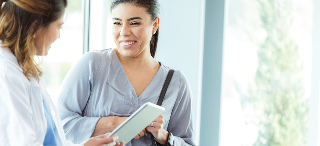 Patient payment plan - A female doctor holding a tablet device while talking to her female patient about flexible payment plans.