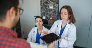 Electronic billing - A female doctor holding a tablet device, asking a male patient to enter his contact information.