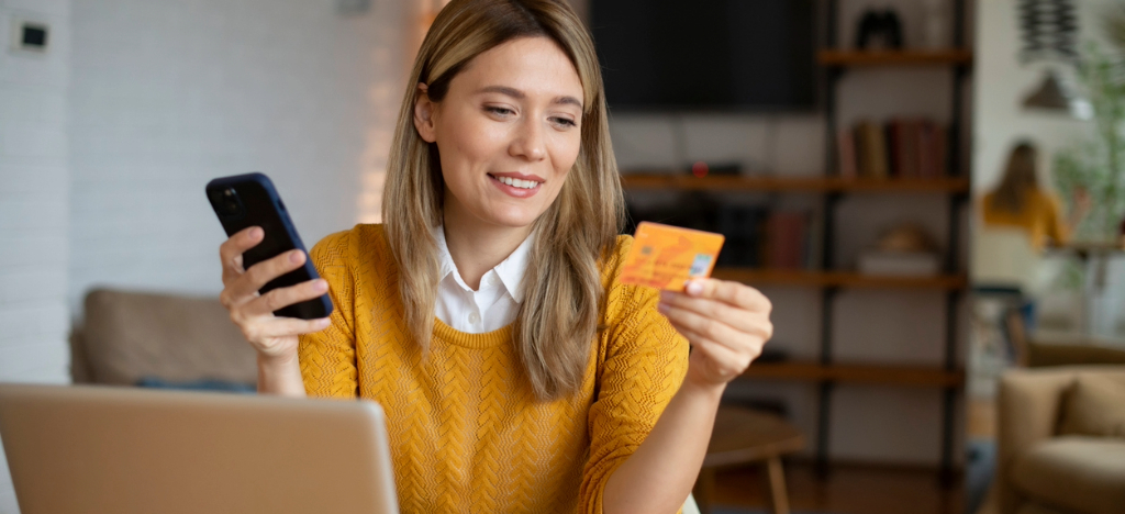 EBPP benefits - A woman at home using her smartphone and credit card to pay for her online bills.