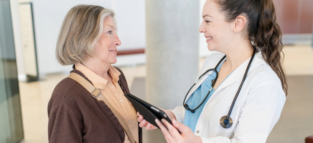 Patient cancellations - A female doctor holding a tablet device while speaking to her female senior patient.