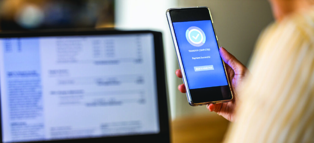 Sending eBill notices to patients - A woman using a smartphone to pay a medical bill that is shown on a laptop screen.