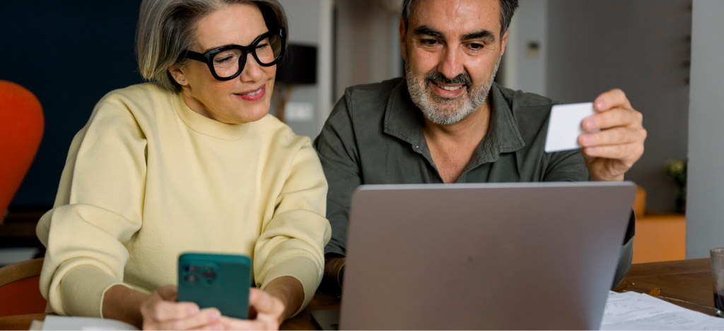A mature couple at home paying their medical bills using their laptop, smartphone, and credit card.