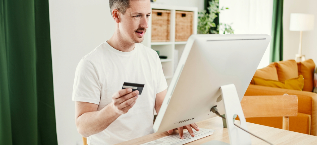 Man using a card to make an online payment from a desktop PC at home.