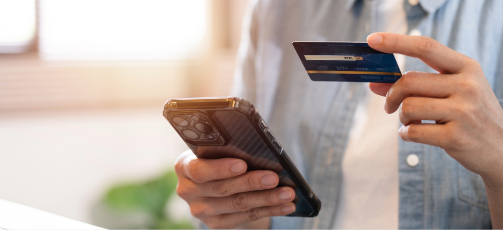 Types of payment methods - A man at home holding his credit card and smartphone while paying for his online medical bill.