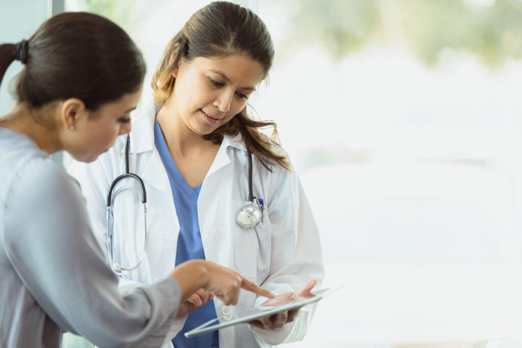 Flexible healthcare payment trends - A female doctor holding a tablet device while discussing payment plans with her patient.