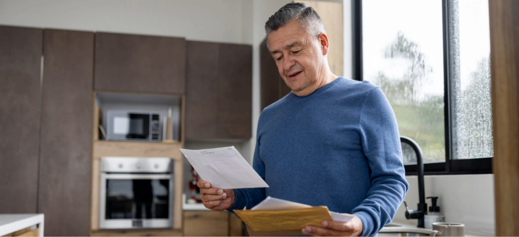 A senior man at home opening his mailed medical bills.