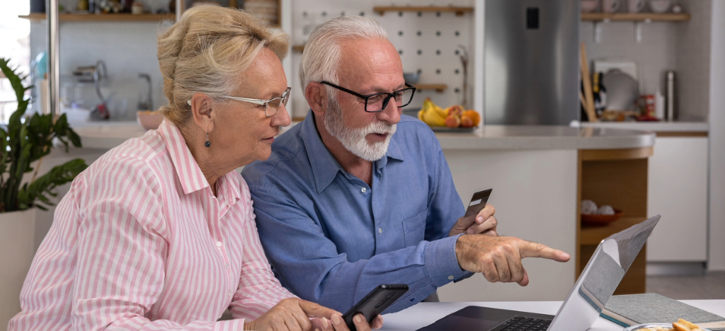 Helping medical office staff - A senior couple at home paying their medical bills online using a smartphone and a laptop.