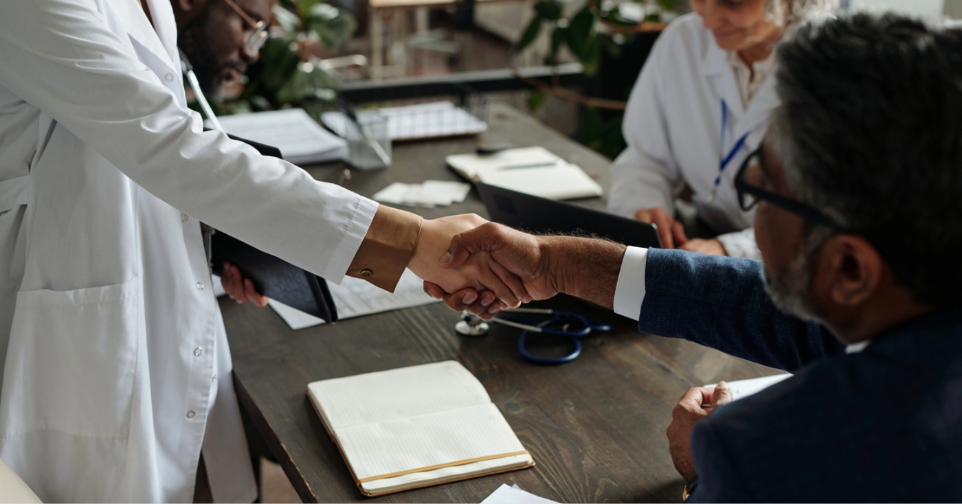 RCM outsourcing companies - A doctor and a businessman shaking hands during a business partnership meeting.
