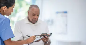 Secure medical credit card processing - A female healthcare staff assisting a senior man in settling his bill using a credit card.