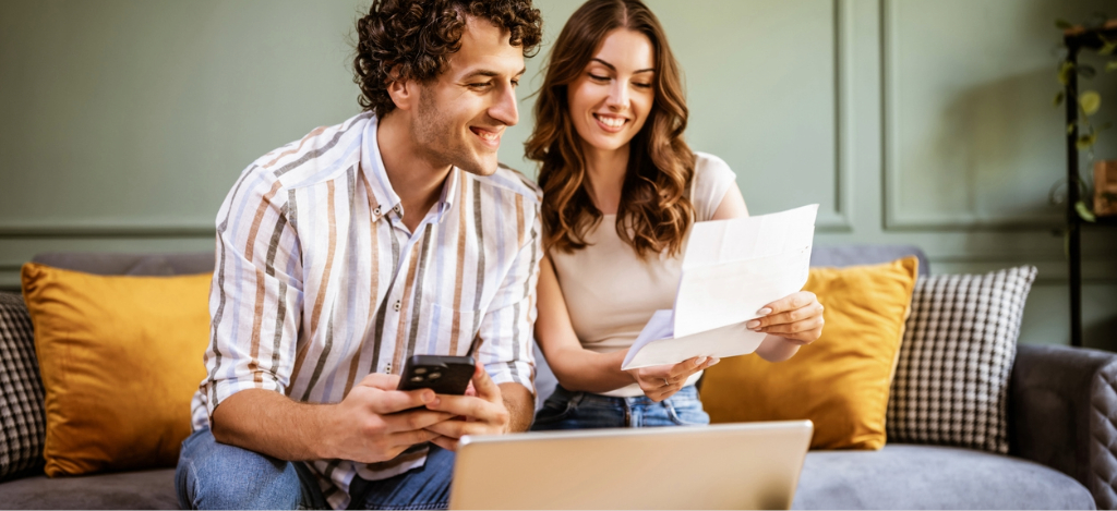 A couple at home paying their hospital bills online using their smartphone and laptop.