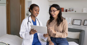 Automatic payment programs - A female doctor showing a tablet device to her female patient.
