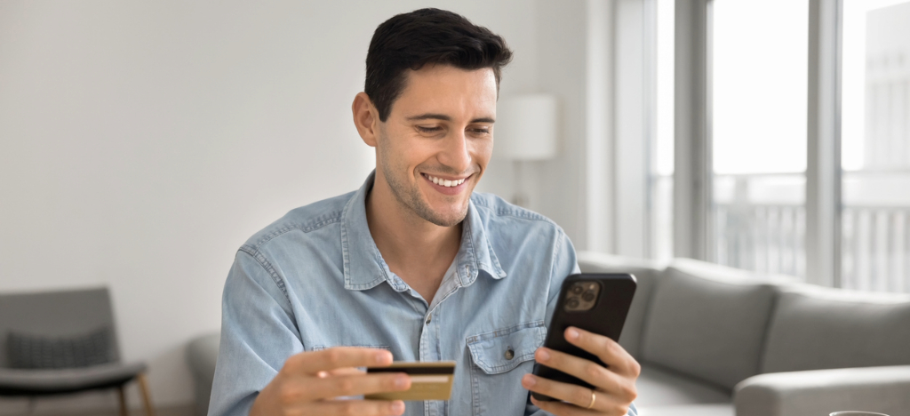 A man at home paying medical bills using his smartphone and credit card.