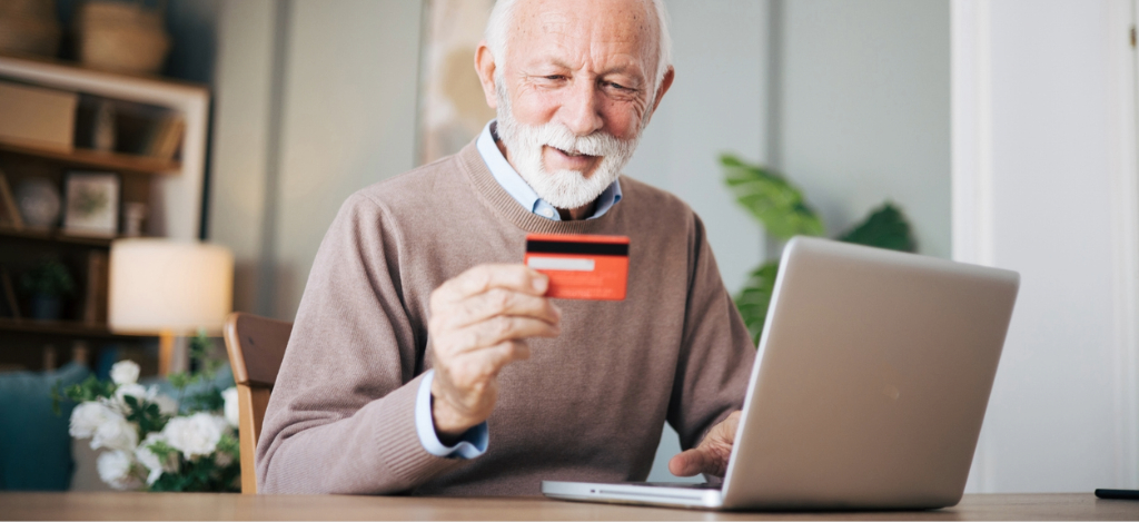 RCM companies - A senior man at home using a laptop and a credit card to settle his medical bill online.