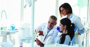 Breaking down costs for patients who can’t afford dental care - A male dentist and his assistant explaining a dental procedure to a female patient.