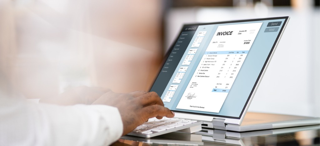 Using automated billing software - A male doctor using a computer while reviewing patient invoices.