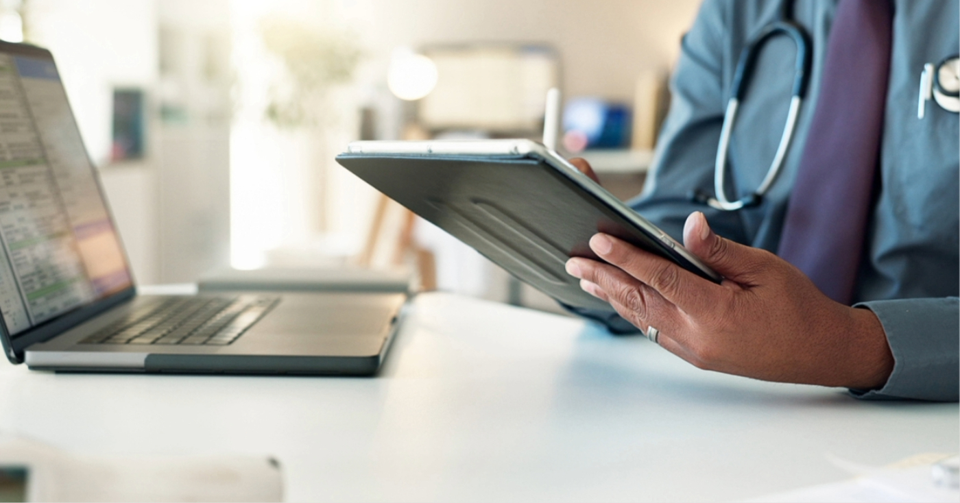EHR integration - A male doctor using a tablet device and a laptop to access their practice’s EHR system.