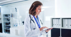RCM companies - A female doctor in a hospital using a tablet device to check her practice’s billing and collection platform.