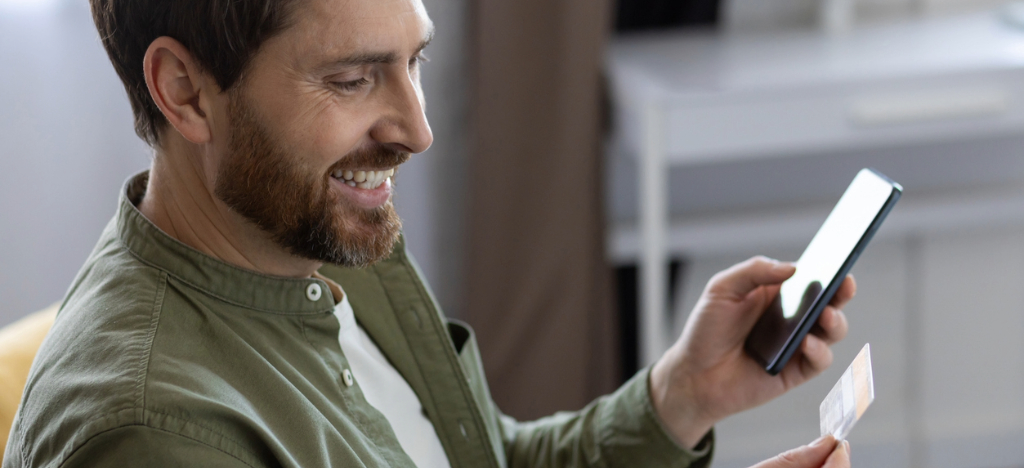 AI medical billing - A man at home using his smartphone and credit card to settle his medical bill online.